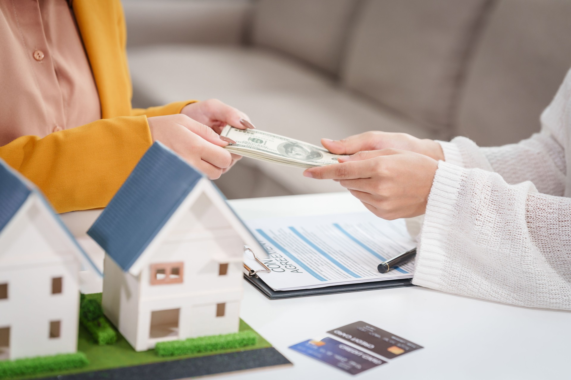 Asian businesswoman discusses home purchase contracts with clients at her desk, focusing on loans, mortgages, and other financial aspects of real estate transactions.